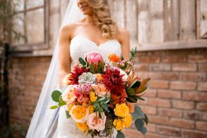 Bride holding red, yellow, orange extravagant bouquet with succulents.
